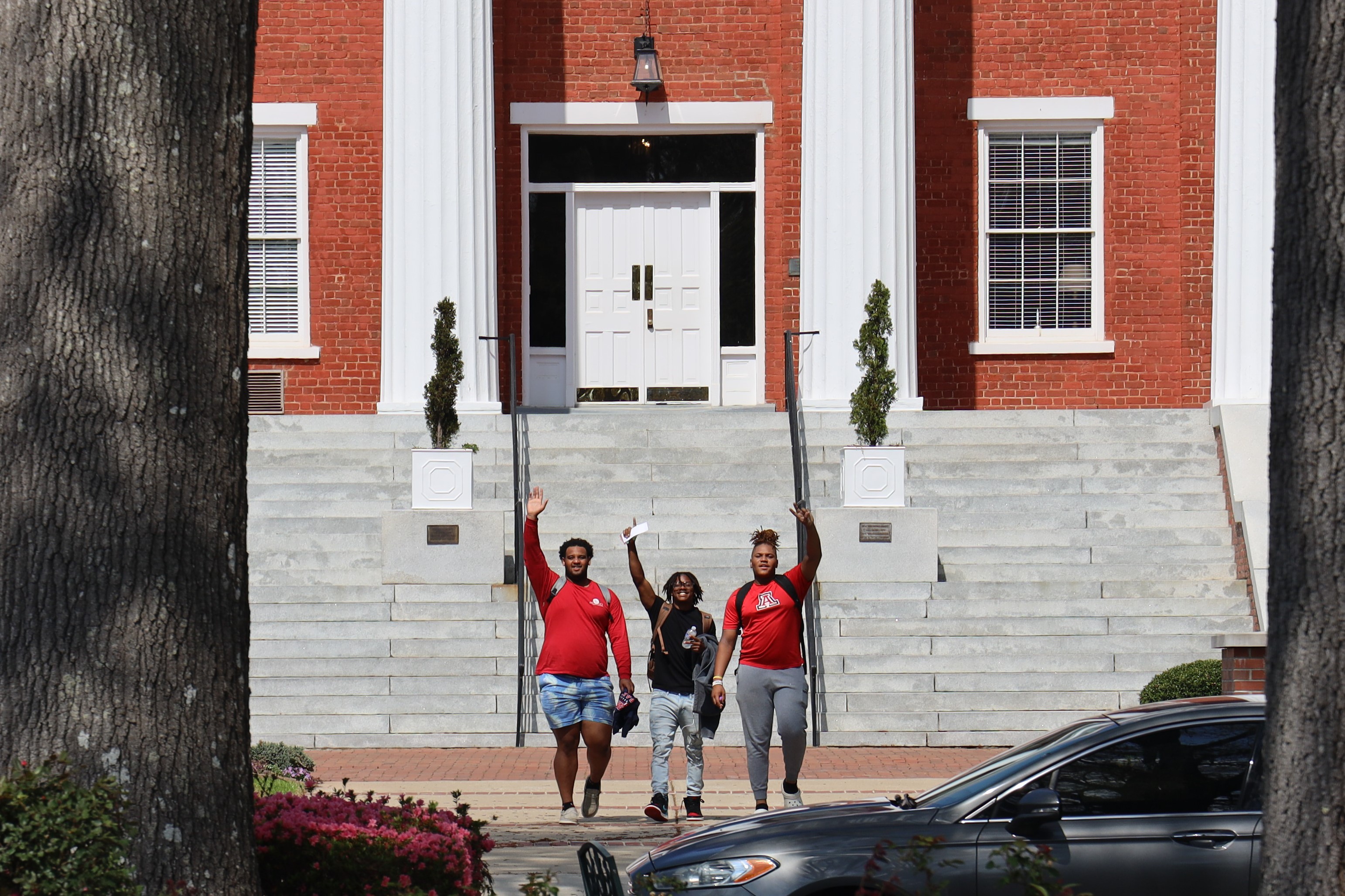 Three Louisburg College students waving to camera in front of Main Building.