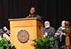 George Lahai stands at the podium while people sit and listen to his speech.