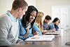 college students are seated beside each other at a table and helping one another study